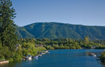 Blue calm lake with docks jutting from shoreline some with pleasure craft green hills are dotted with homes against backdrop of mountains and blue sky Lake Cowichan Vancouver Island BC Canada