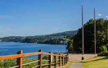 Gravel pathway in foreground leading down to clear area with two tall poles a fence lies between this area and the blue water with residential hills in background against blue sky Ladysmith Vancouver Island BC Canada.