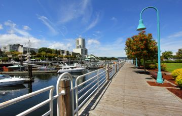 Boardwalk with gardens on one side with light stand and ocean marina on other side apartment building in background with clear blue sky Nanaimo Vancouver Island BC Canada