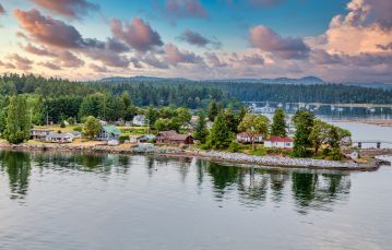 Homes along rocky shoreline with calm ocean waters in foreground and blue sky with pink clouds in background Nanaimo Vancouver Island BC Canada