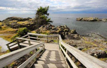 Wood stairway leading down to rocky point next to grey ocean shoreline Nanaimo Vancouver Island BC Canada