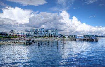 Calm blue ocean shoreline in front of a pier and walkway next to a multi story hotel located in Sidney in Southern Vancouver Island 