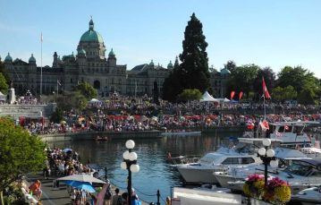 Large crowd gathers for cultural event at Inner Harbour in downtown Victoria with Parliament Buildings in background.