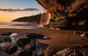 Sandy beach set against eroded cliff at dawn with ocean at low tide in background of southern Vancouver Island