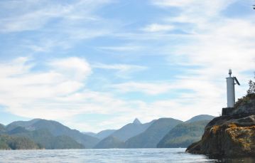 Shoreline of Bligh Island Marine Provincial Park in Nootka sound looking towards mountain range and blue sky in central Vancouver Island British Columbia Canada.