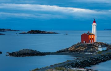 Red and white lighthouse set on rocky point in pacific ocean near Victoria BC at evening time